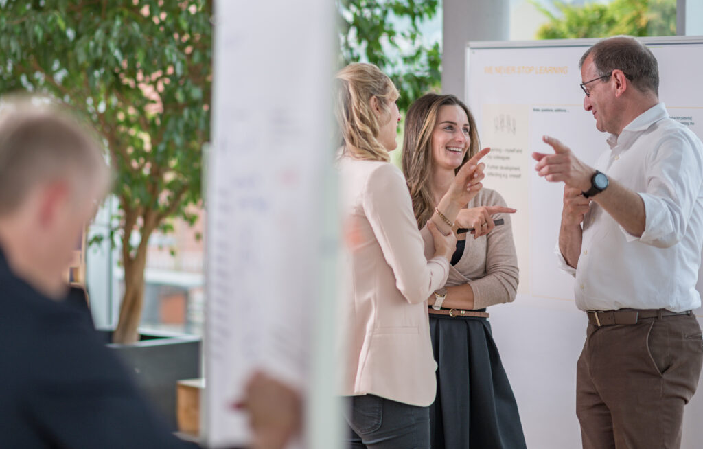 Drei lächelnde Personen, die in einem Raum miteinander reden