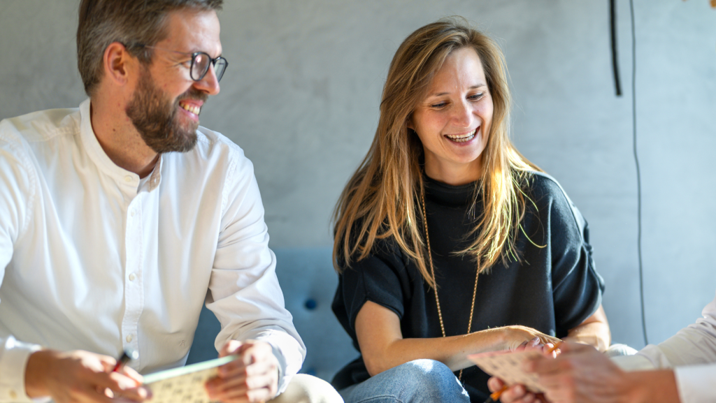 Lachende Frau und Mann sitzen, die auf eine Notiz in der Hand von einer nicht sichtbaren person schauen