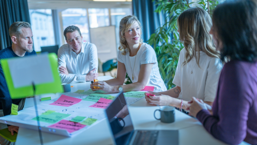 Group of people siiting at a table with notebook and postits on poster