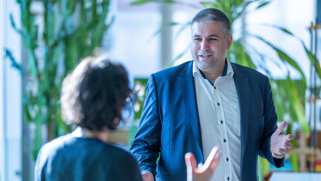 Mann in Hemd und Sakko im Gespräch mit Frau, die man von hinten sieht