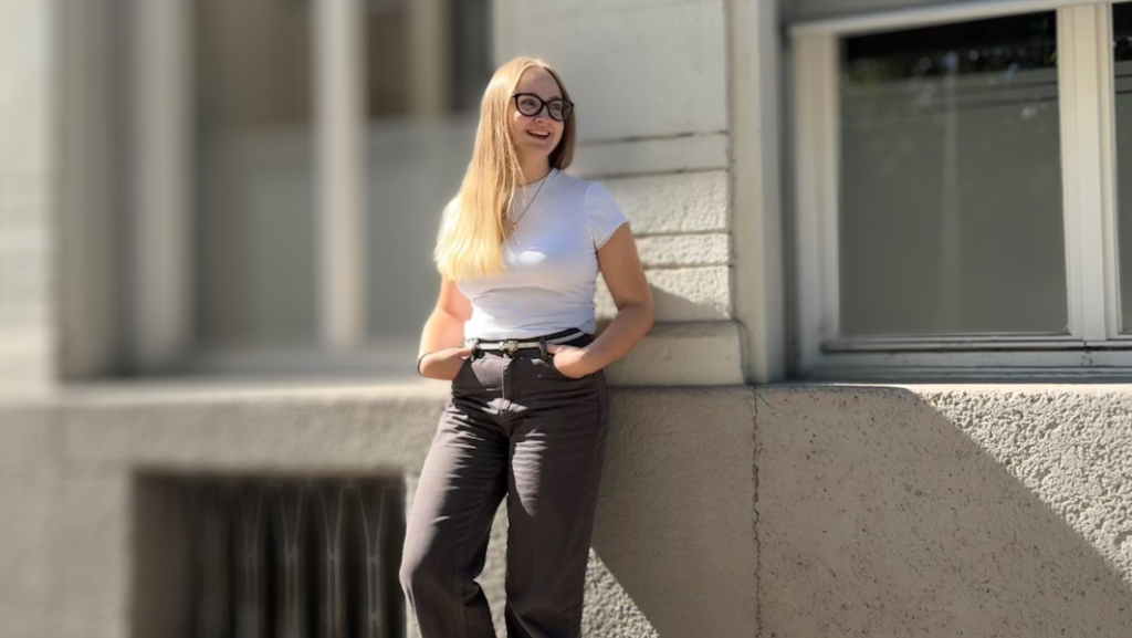 Lachende, blonde junge Frau an hausmauer gelehnt